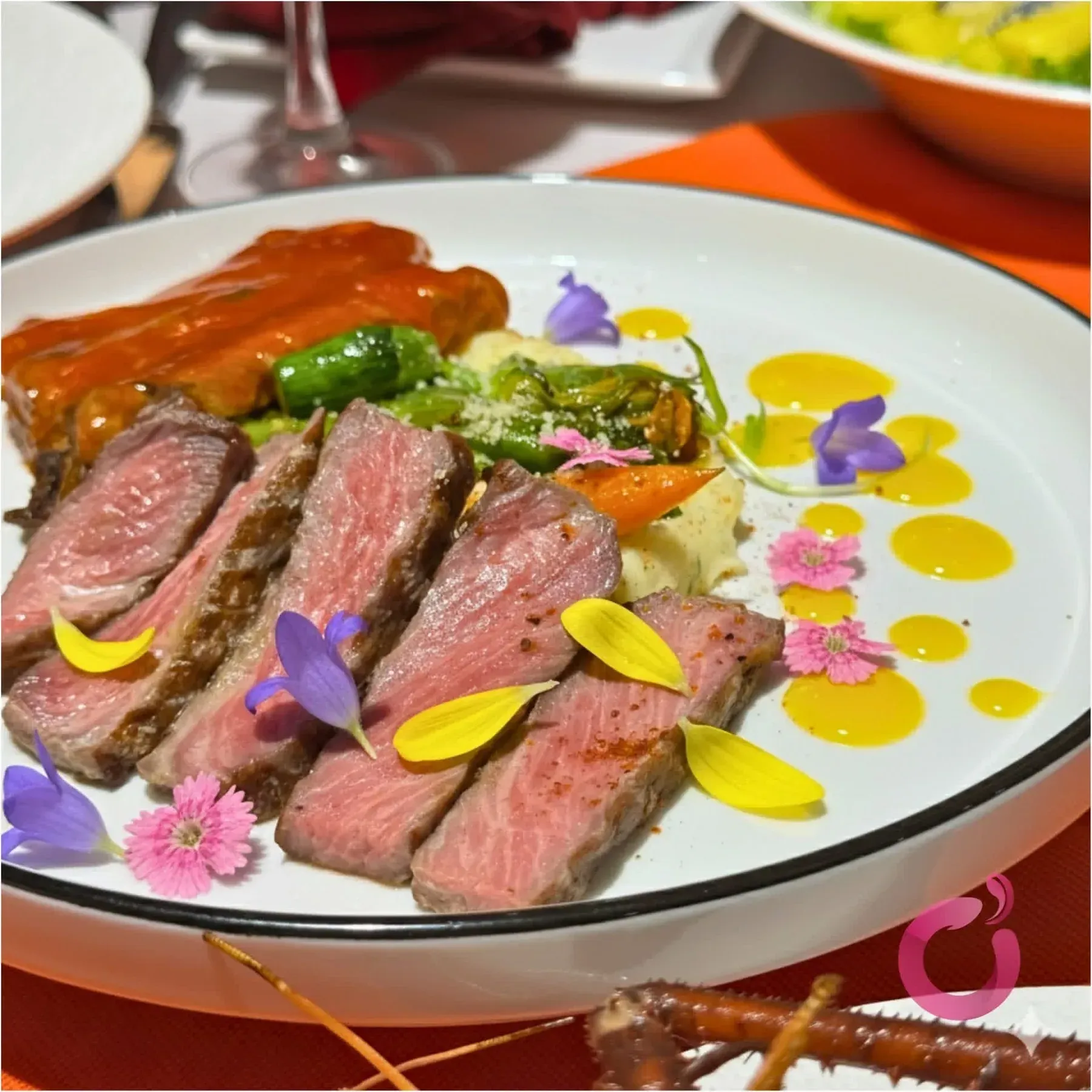 Đĩa steak bò cắt lát chín hồng trang trí hoa ăn được tại Ơ Bistro